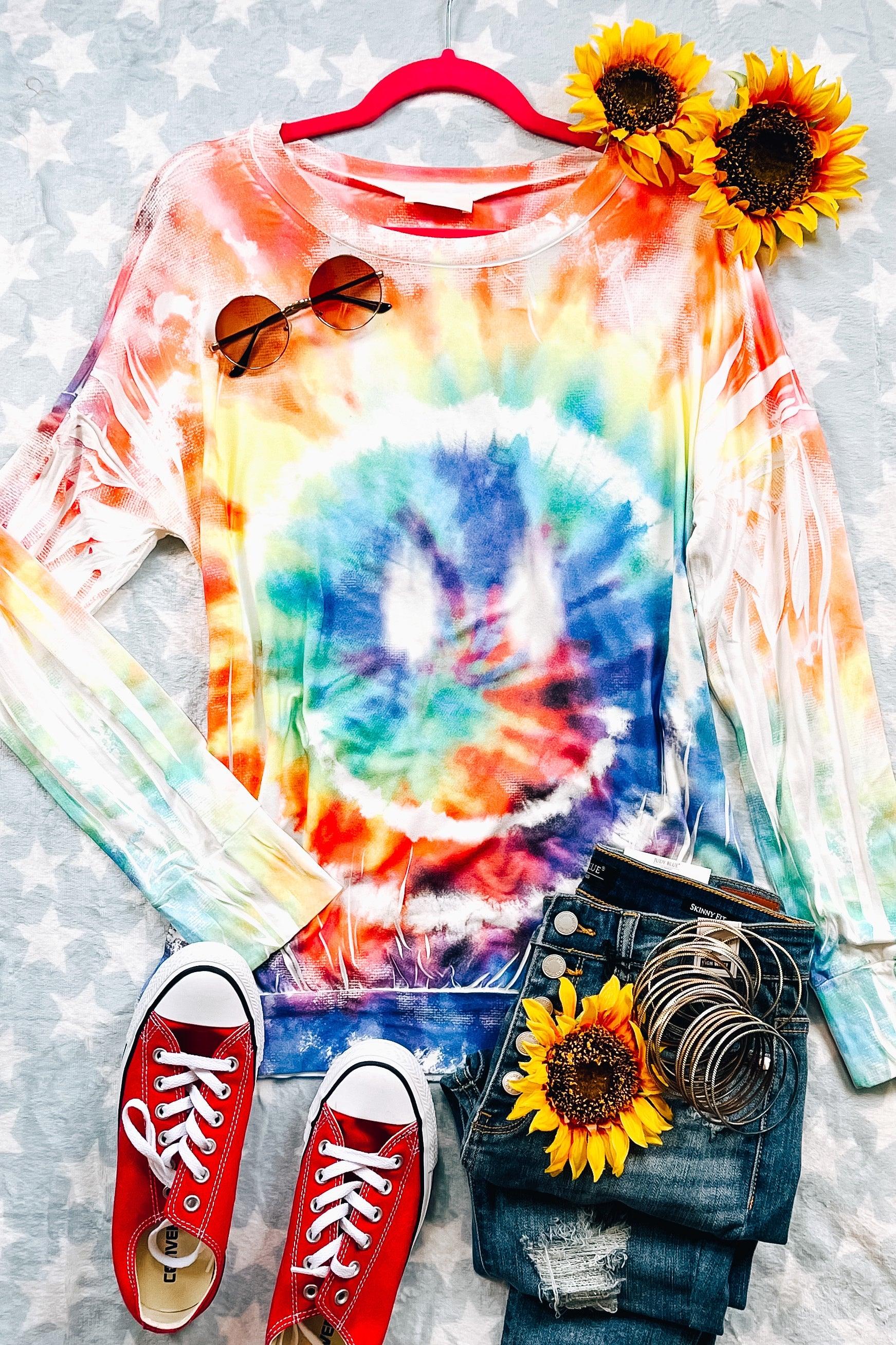 Long-sleeve tie dye pullover with smiley face design paired with distressed jeans, red canvas shoes, and sunglasses
