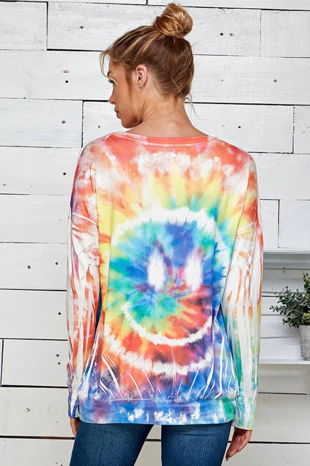 Woman wearing a colorful tie dye pullover with a large smiley design in a casual, relaxed fit, styled with jeans