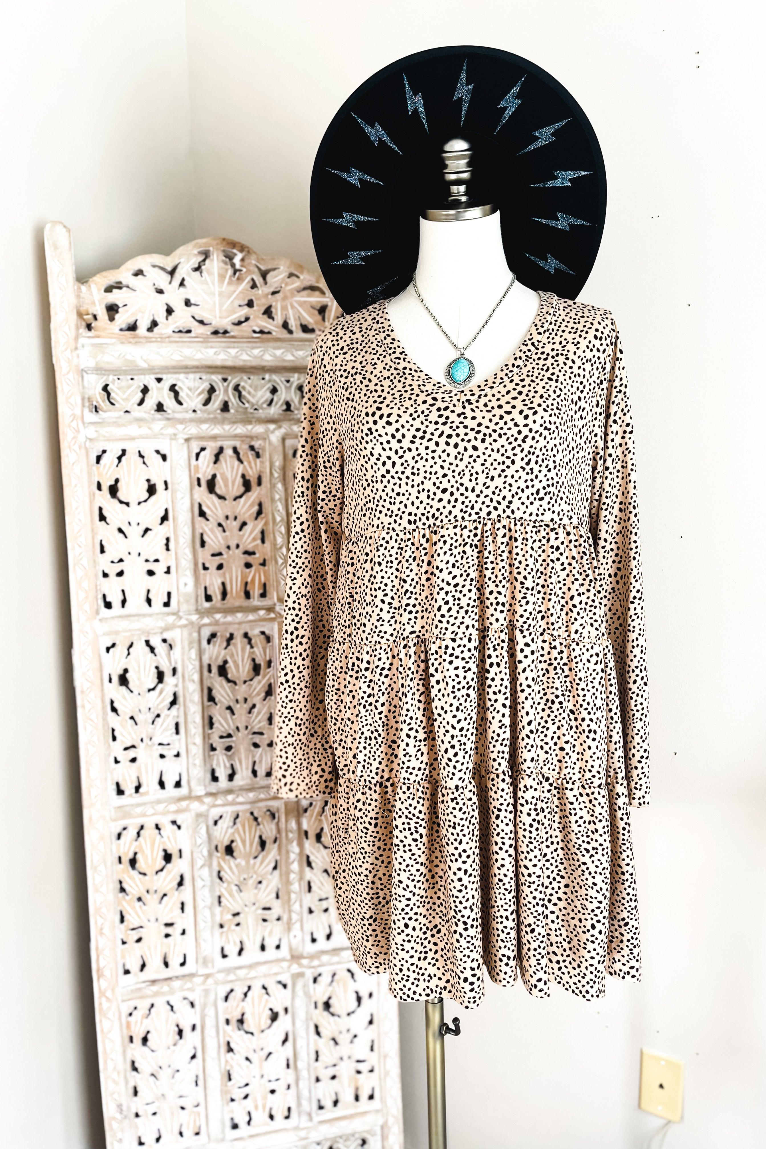 Taupe animal print dress with V neckline and flowing tiered skirt displayed on mannequin with black hat and turquoise necklace