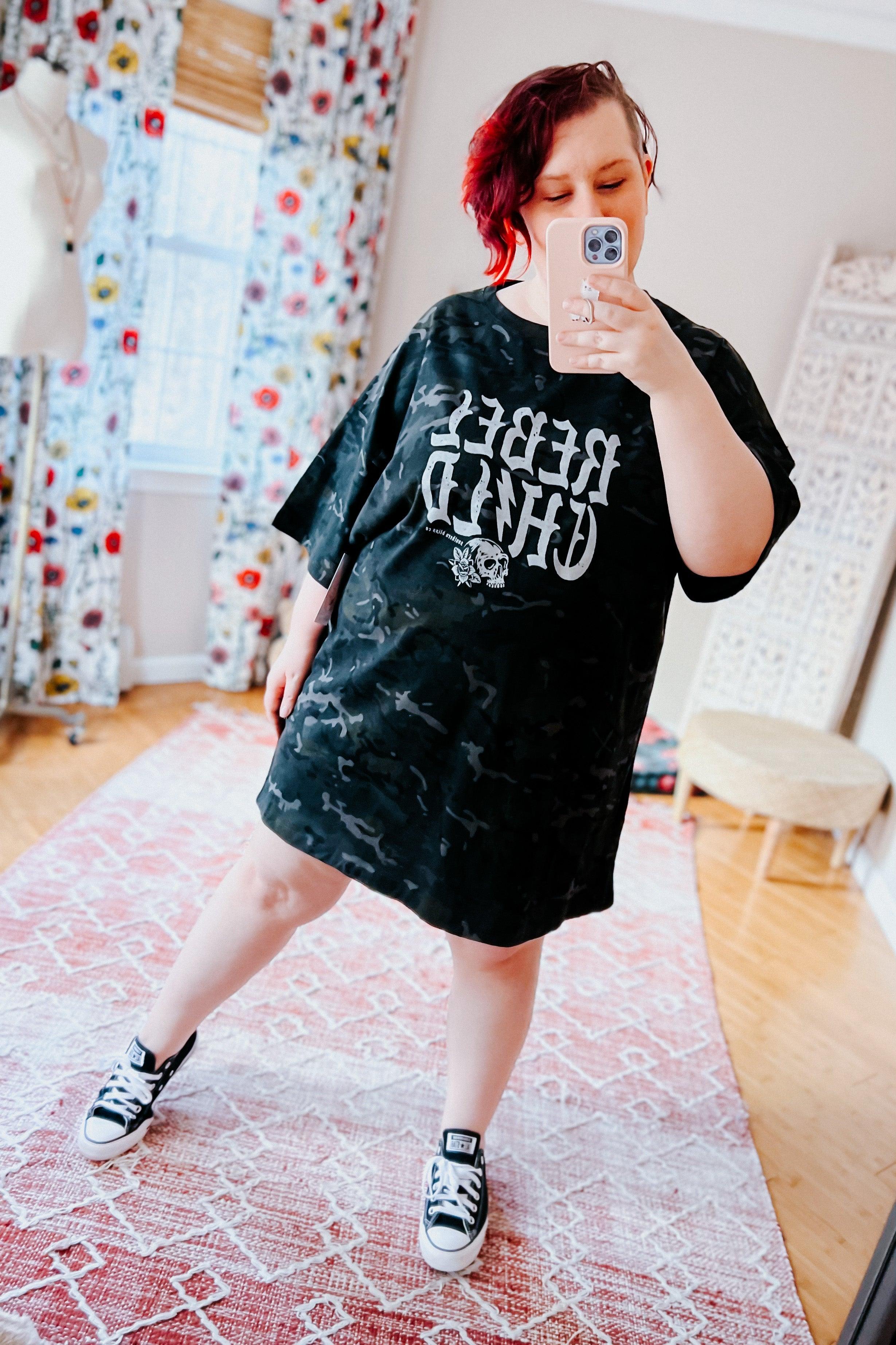 Woman taking mirror selfie wearing black camo oversized tee with bold skull graphic styled with casual sneakers indoors