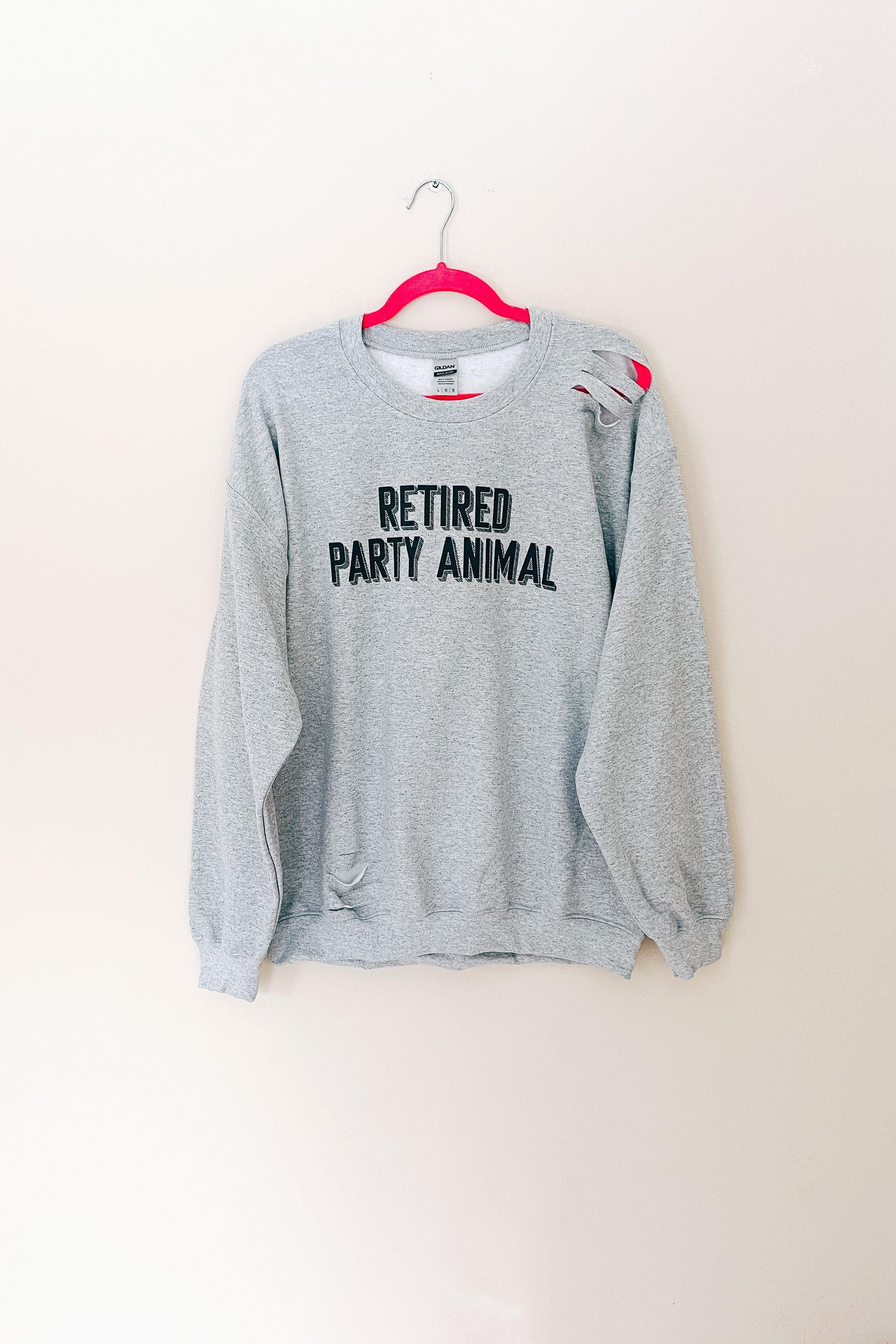 Grey distressed pullover with bold black text and intentional rips displayed on bright pink hanger against white wall