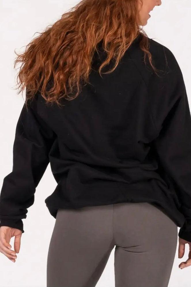 Woman with long red hair wearing black oversized organic cotton sweatshirt and gray leggings from behind