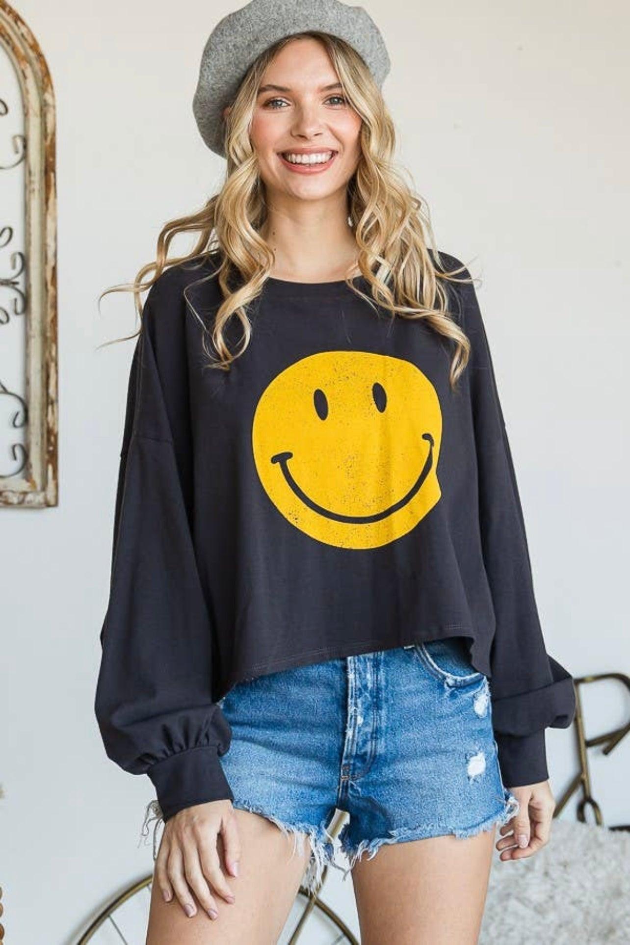 Woman wearing charcoal long sleeve crop top with yellow smiley face paired with distressed denim shorts and gray beret