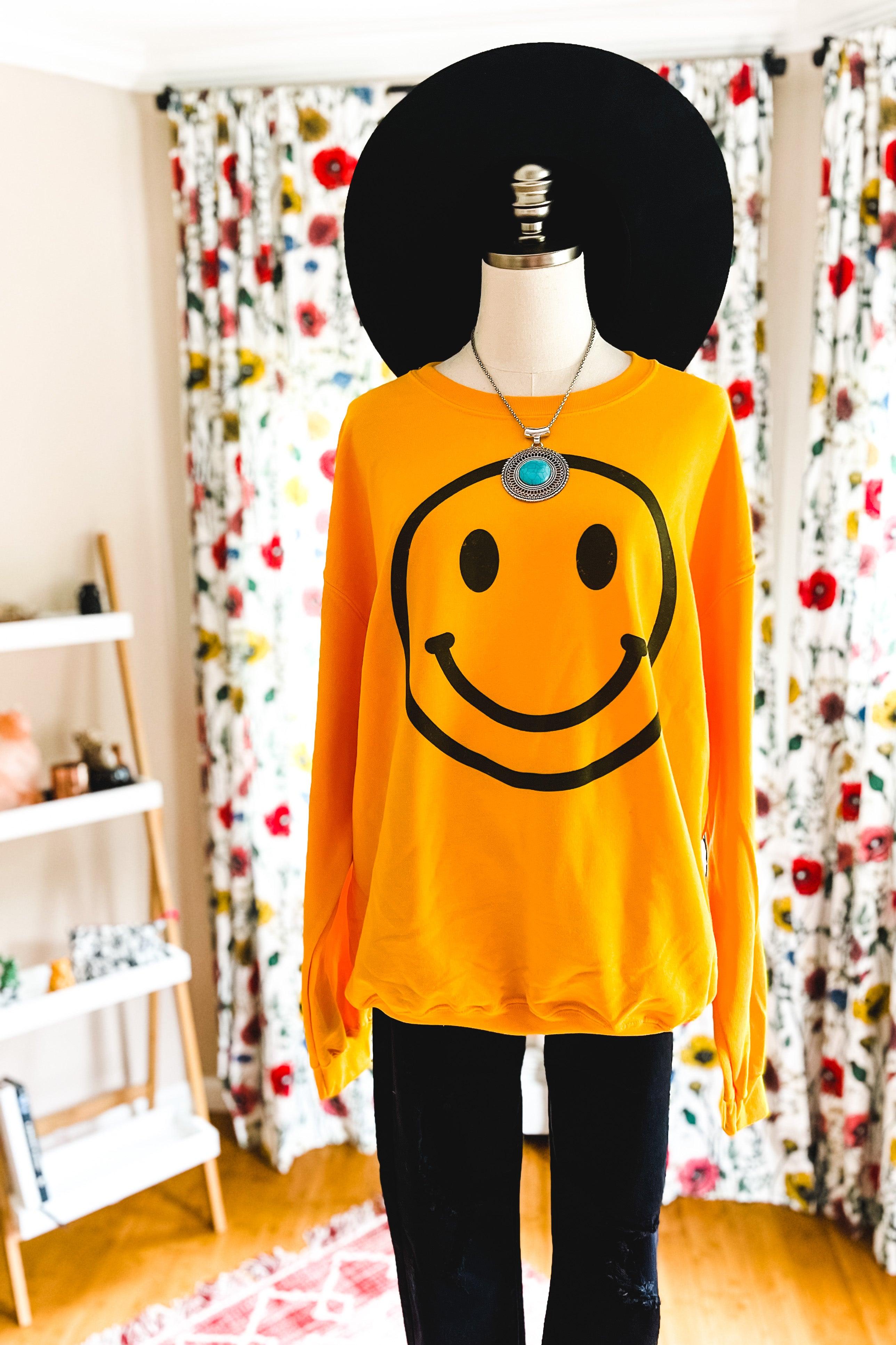 Yellow sweatshirt with large black smiley face graphic styled with turquoise pendant necklace and black hat on mannequin