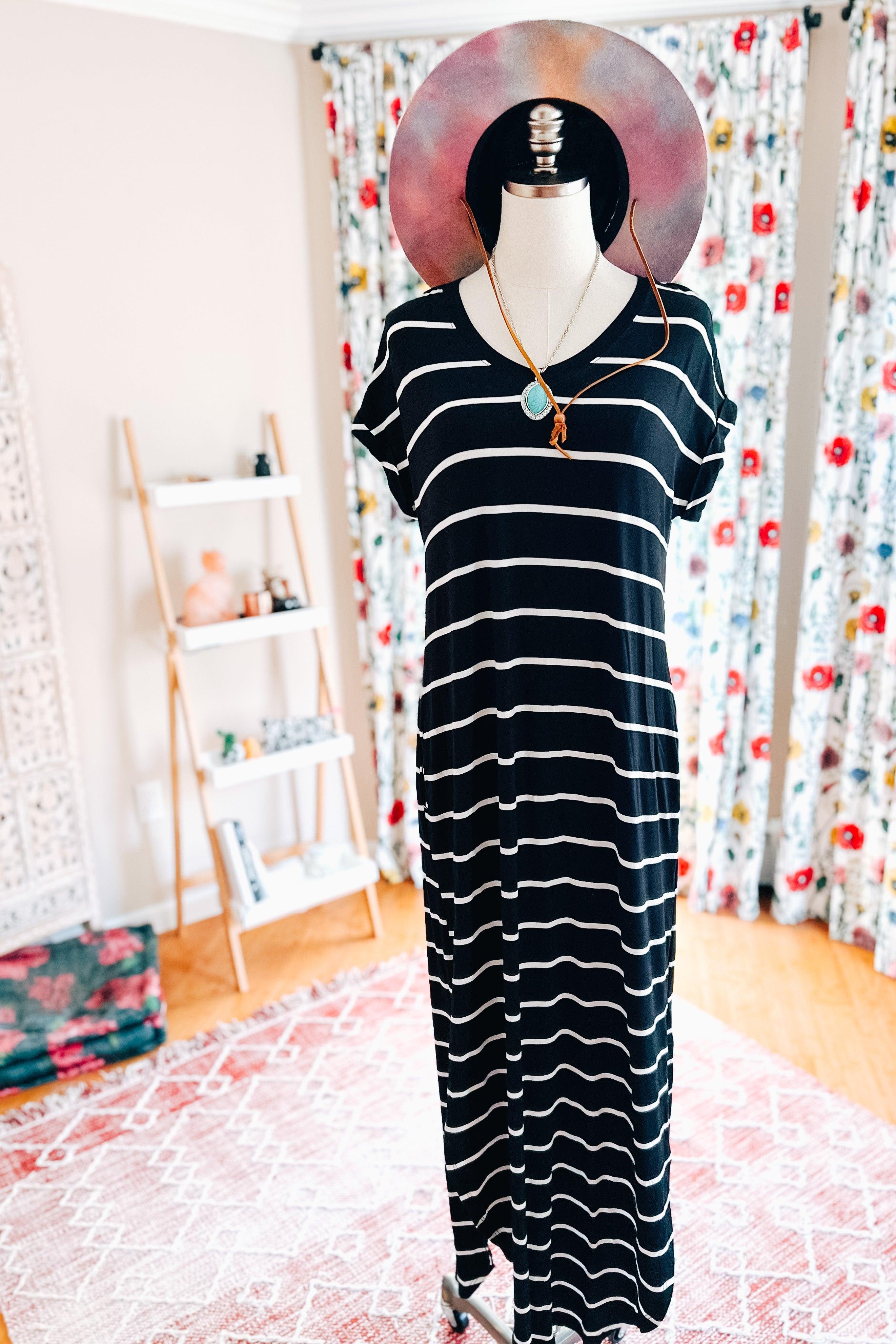 Black and white striped maxi dress displayed on mannequin wearing colorful wide-brimmed hat in cozy room setting