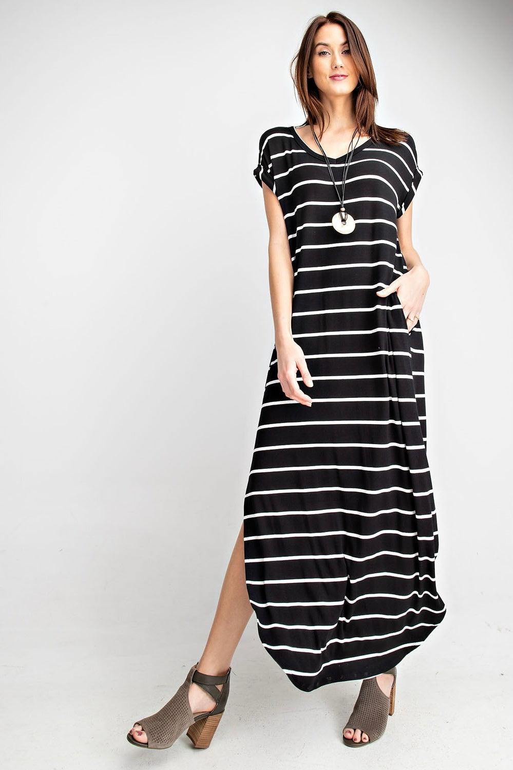 Woman wearing black maxi dress with white stripes and cutout heeled ankle boots standing against white backdrop
