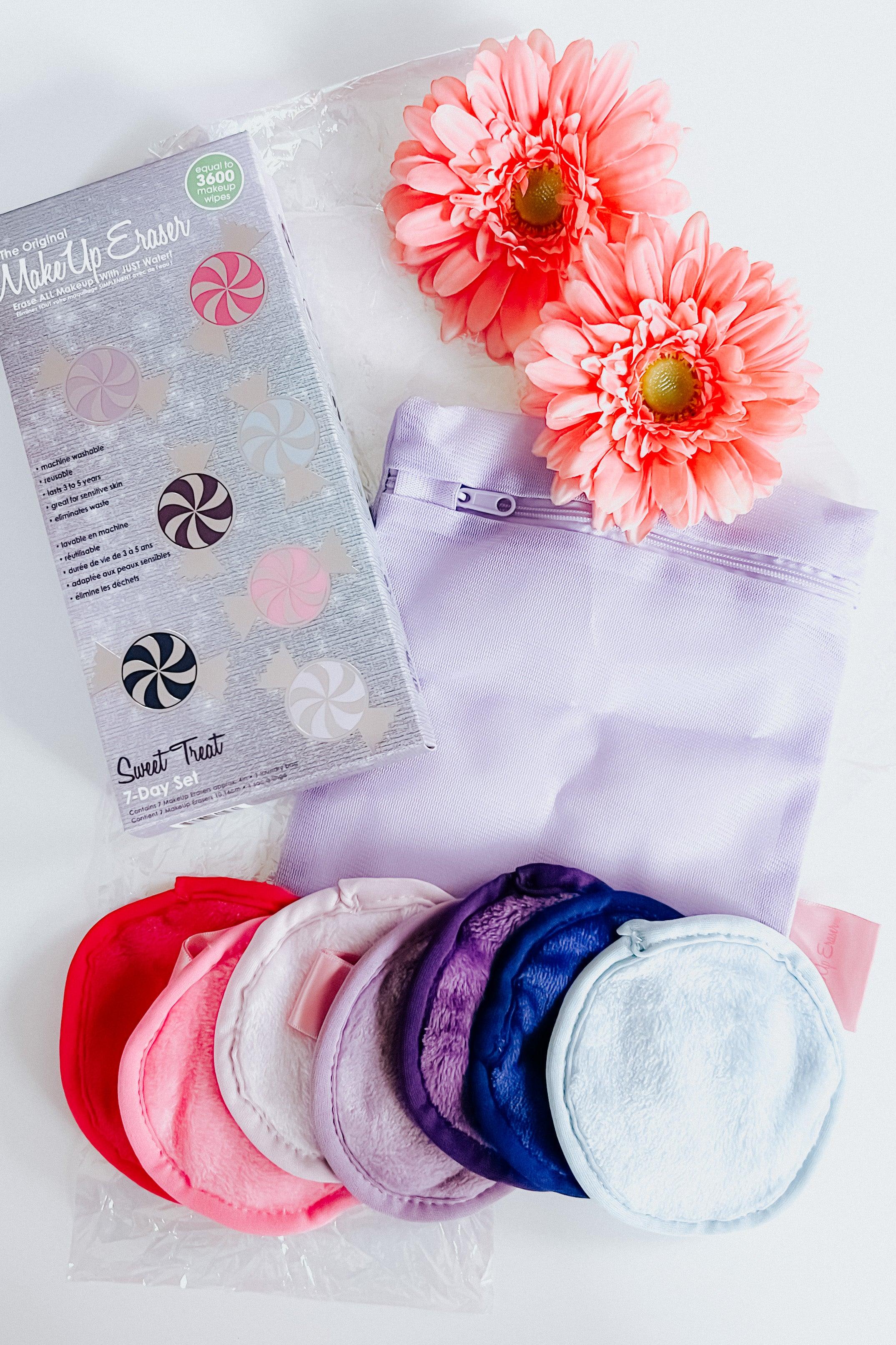 Seven circular plush makeup remover cloths in pink, purple, and blue shades beside a lavender bag and two coral flowers