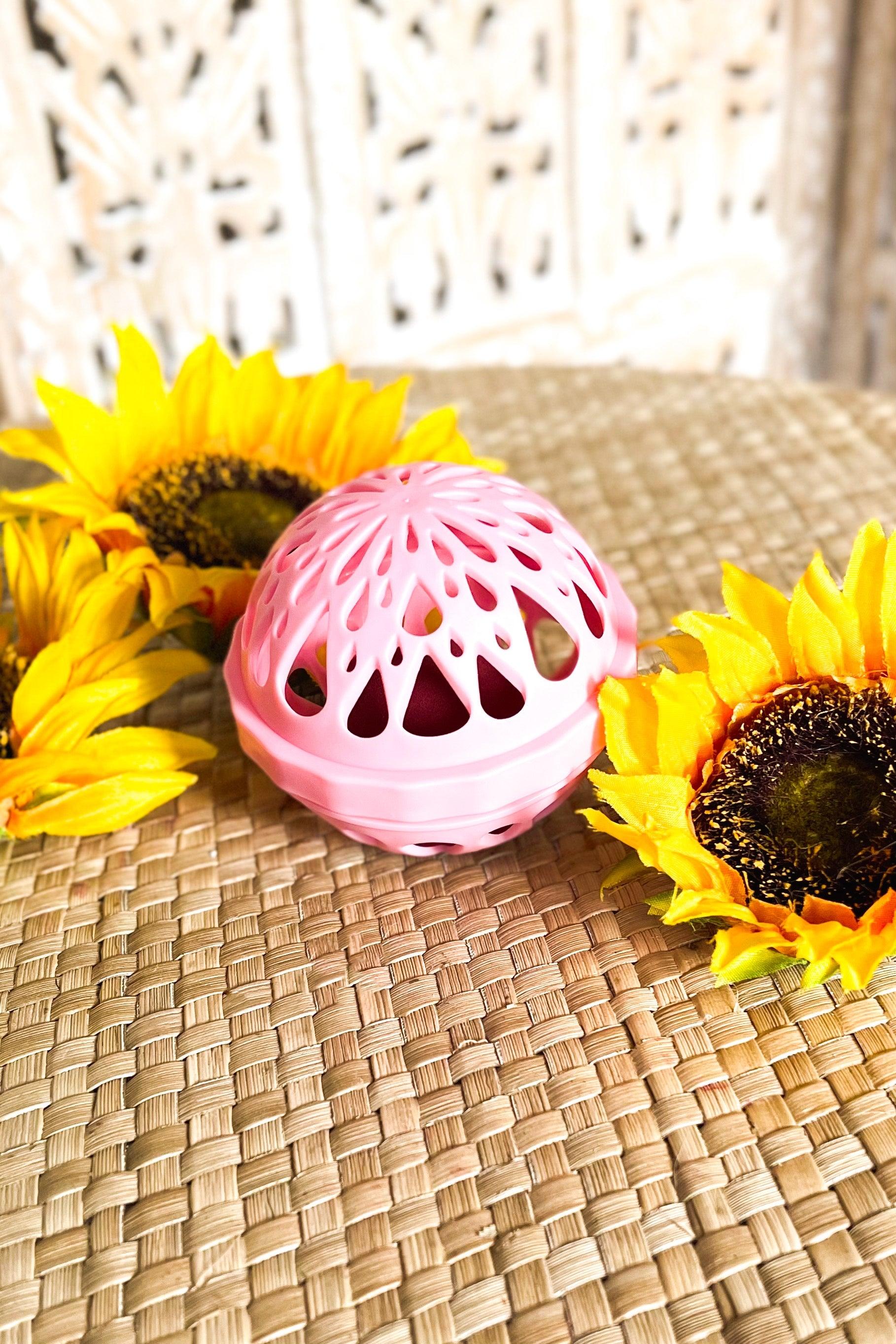 Pink ventilated spherical container set on woven surface with vibrant yellow sunflowers arranged around it