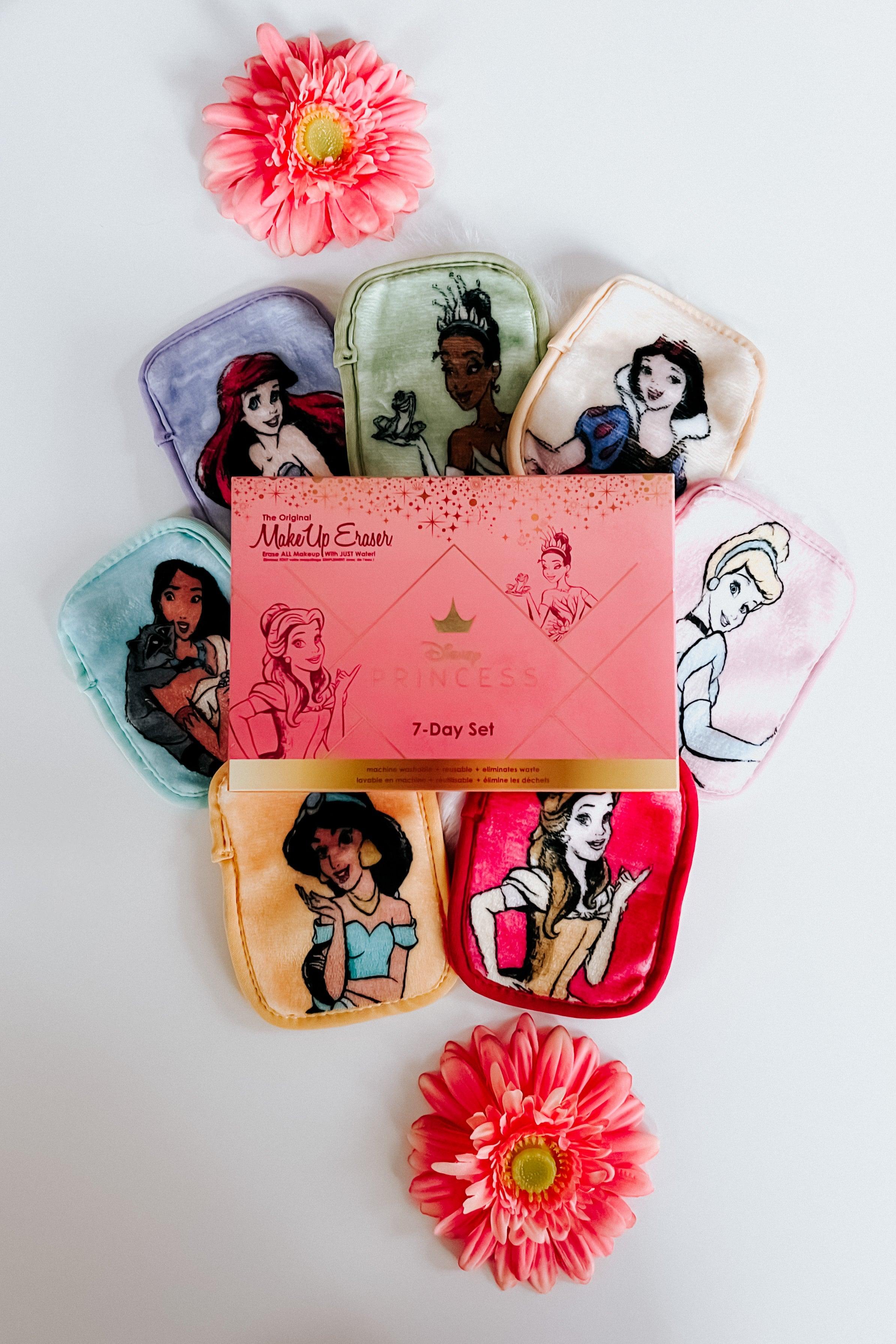 Seven colorful plush makeup eraser pouches featuring Disney princesses arranged around pink flowers on white background