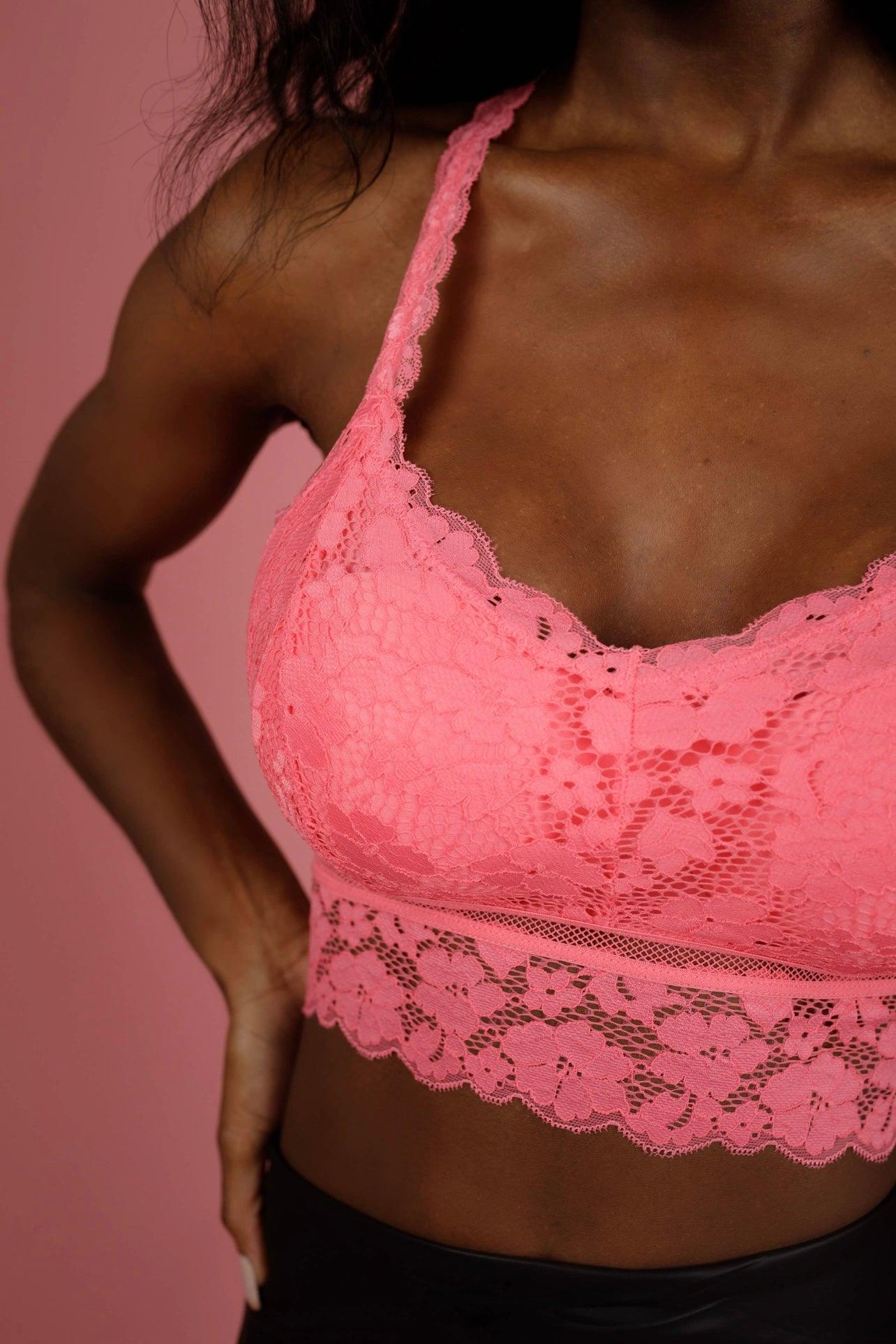 Close-up of a woman wearing a pink lace bralette with floral pattern and scalloped edges in a soft light setting