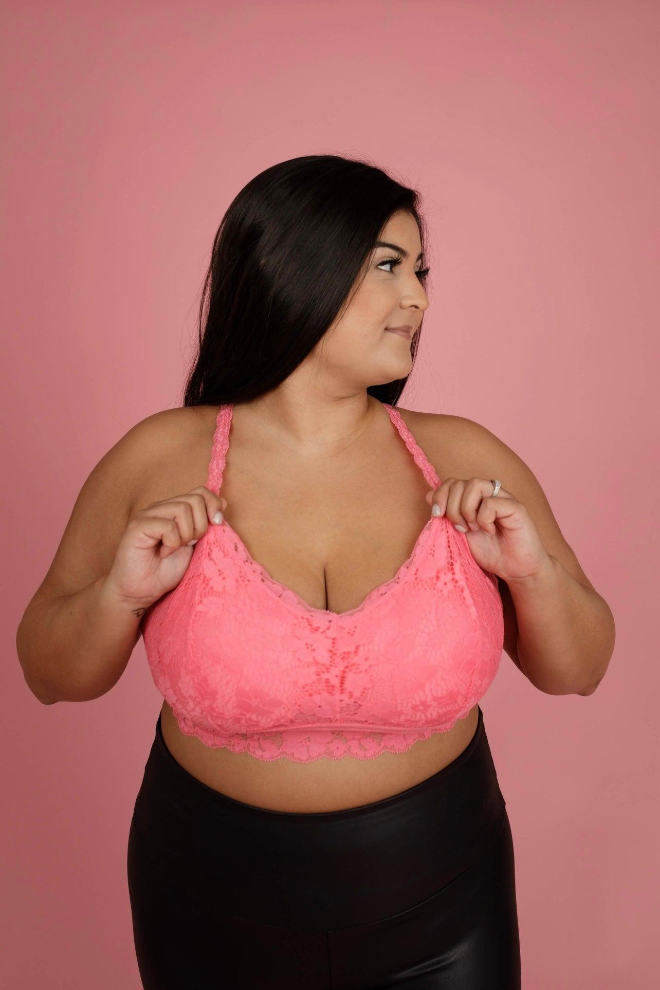 Curvy woman wearing a pink lace bralette with braided straps and black high-waisted pants against a pink backdrop