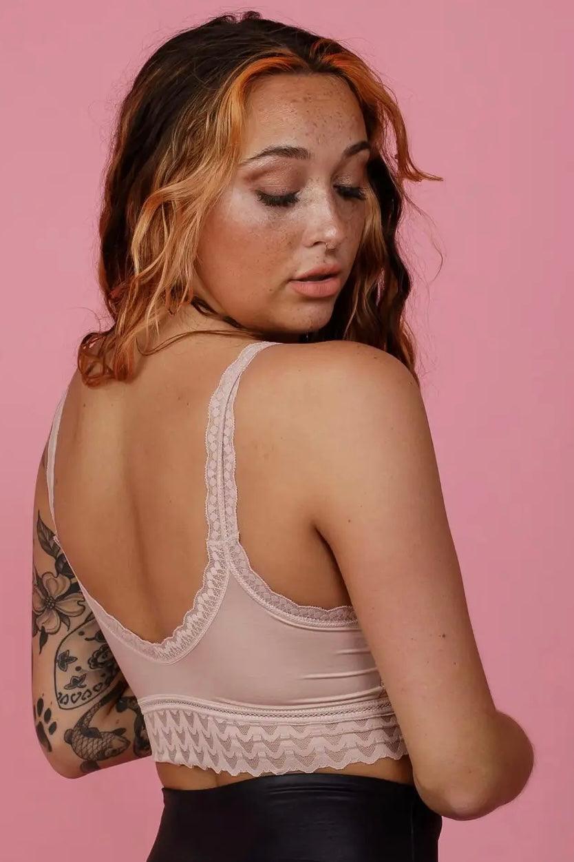 Woman with wavy hair wearing a pink lace bralette with low back and patterned band against pink backdrop