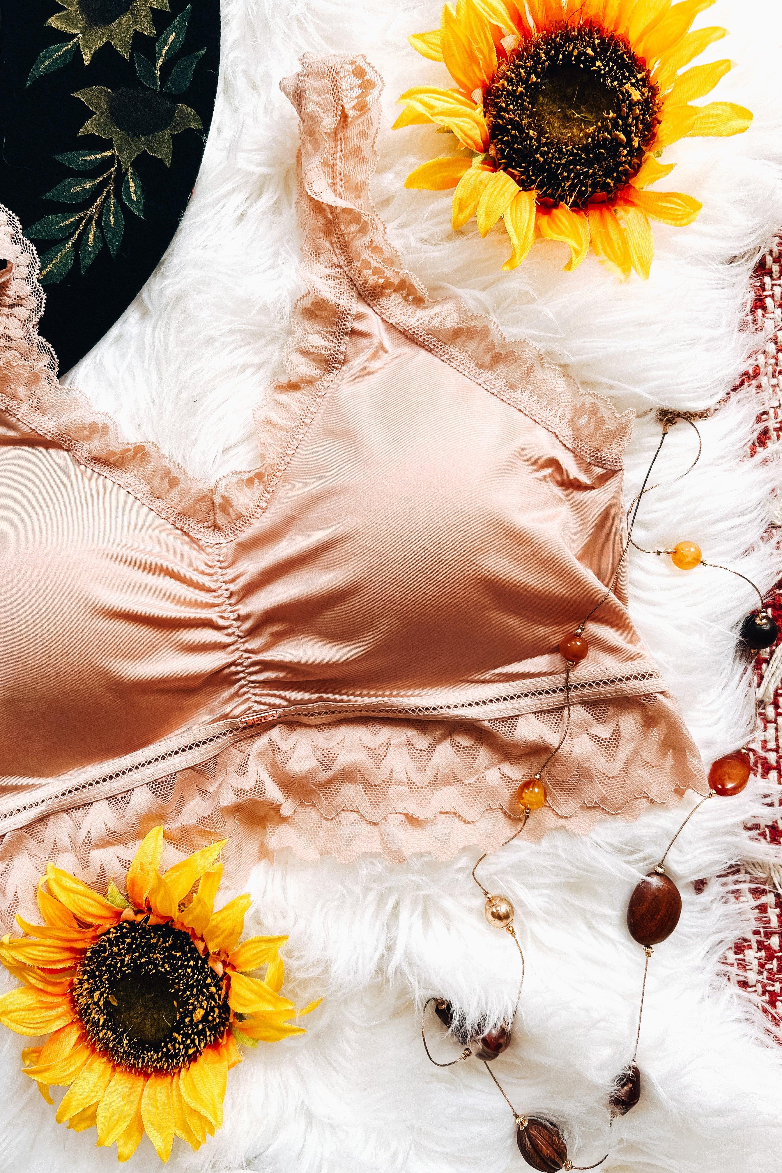 Pink lace bralette with ruched front detail displayed on white fur with sunflowers and beaded necklace