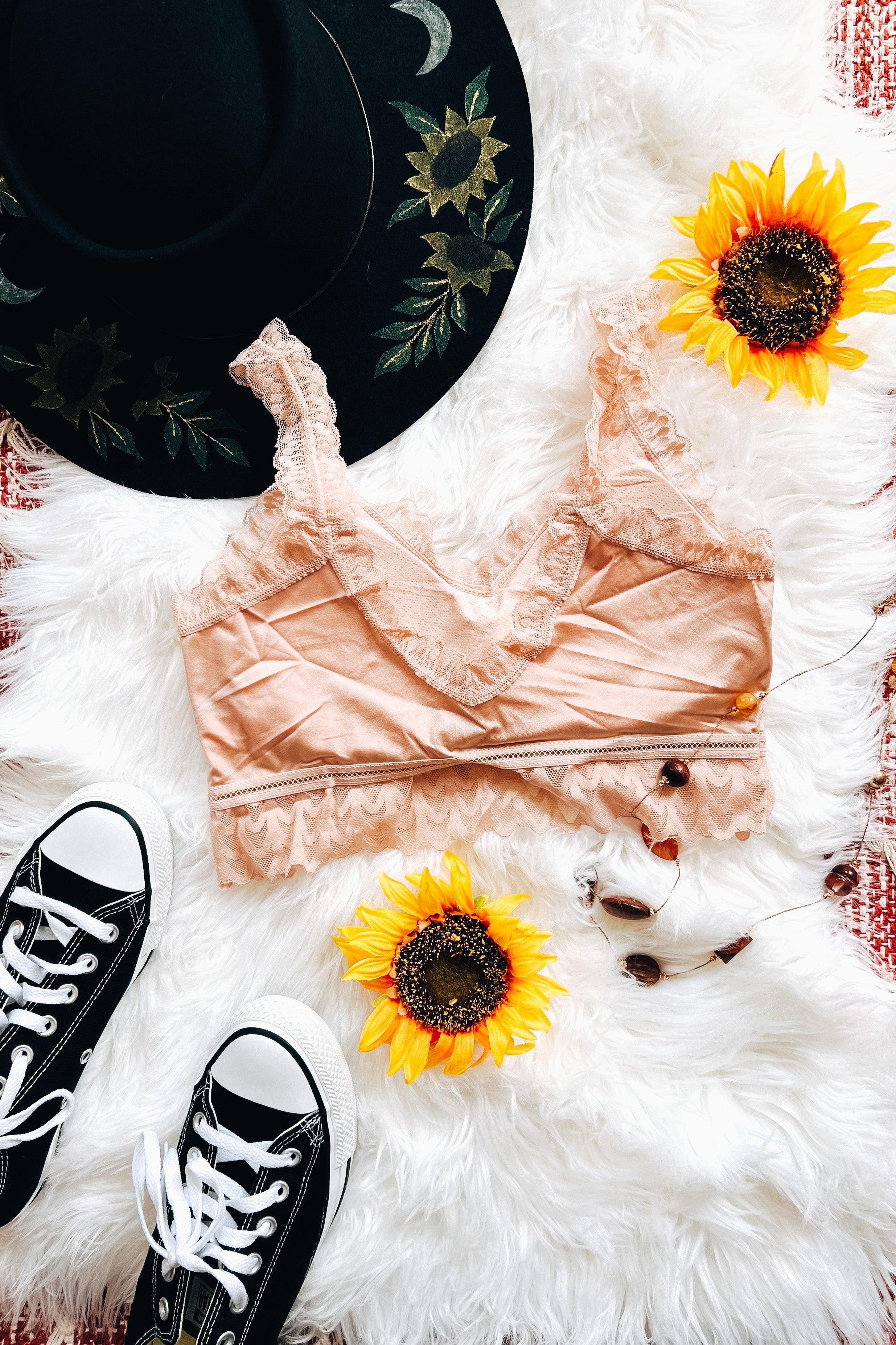 Pink lace bralette styled with floral embroidered black hat, sunflower accents, black sneakers, and vintage sunglasses on white fur