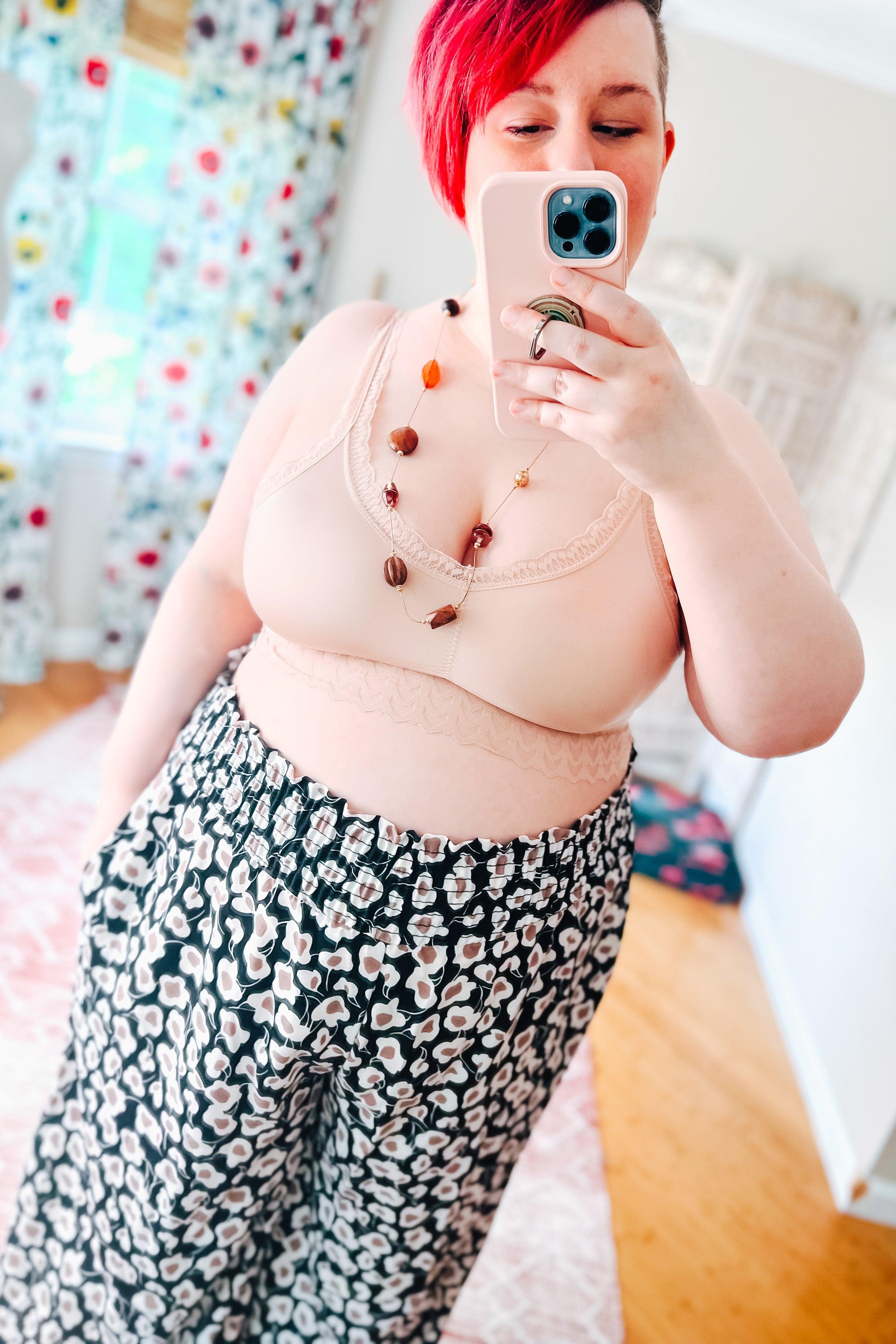 Plus-size woman wearing a soft pink bralette with lace detailing and patterned high-waisted pants in a bright room
