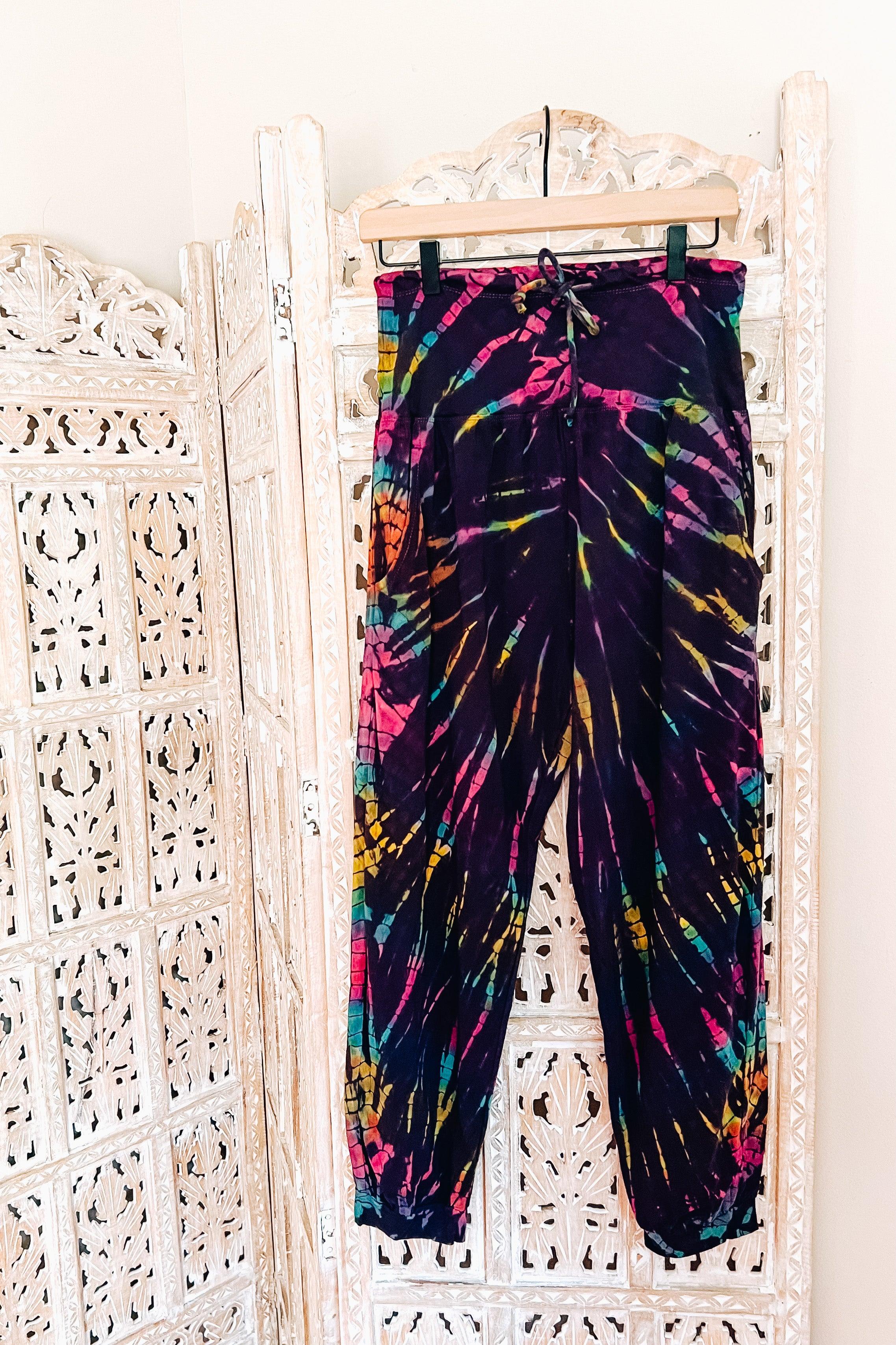 Purple tie-dye joggers with drawstring waist hanging on decorative carved white wooden screen backdrop
