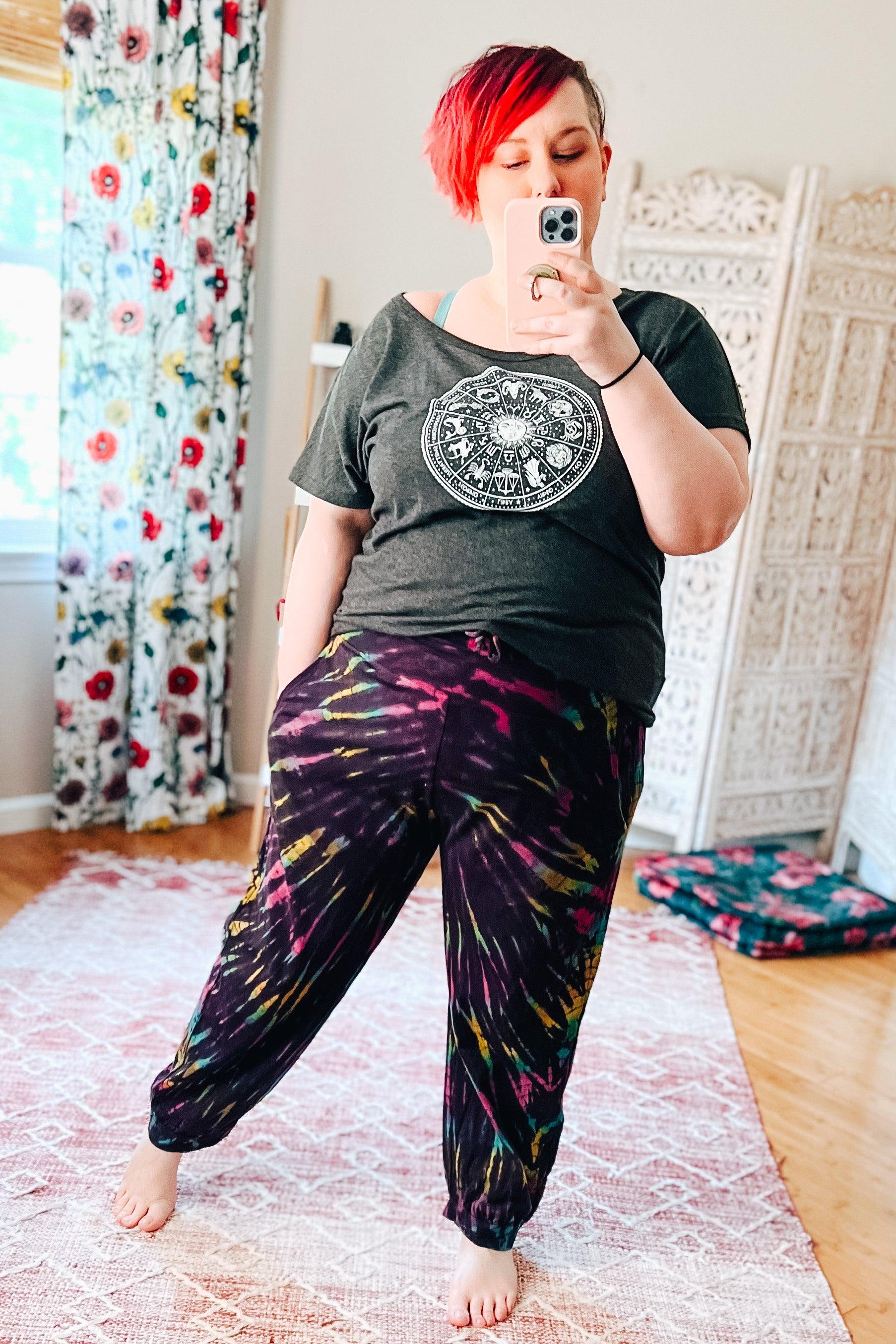 Woman with red hair wearing relaxed purple passion tie dye joggers and dark graphic tee taking indoor mirror selfie