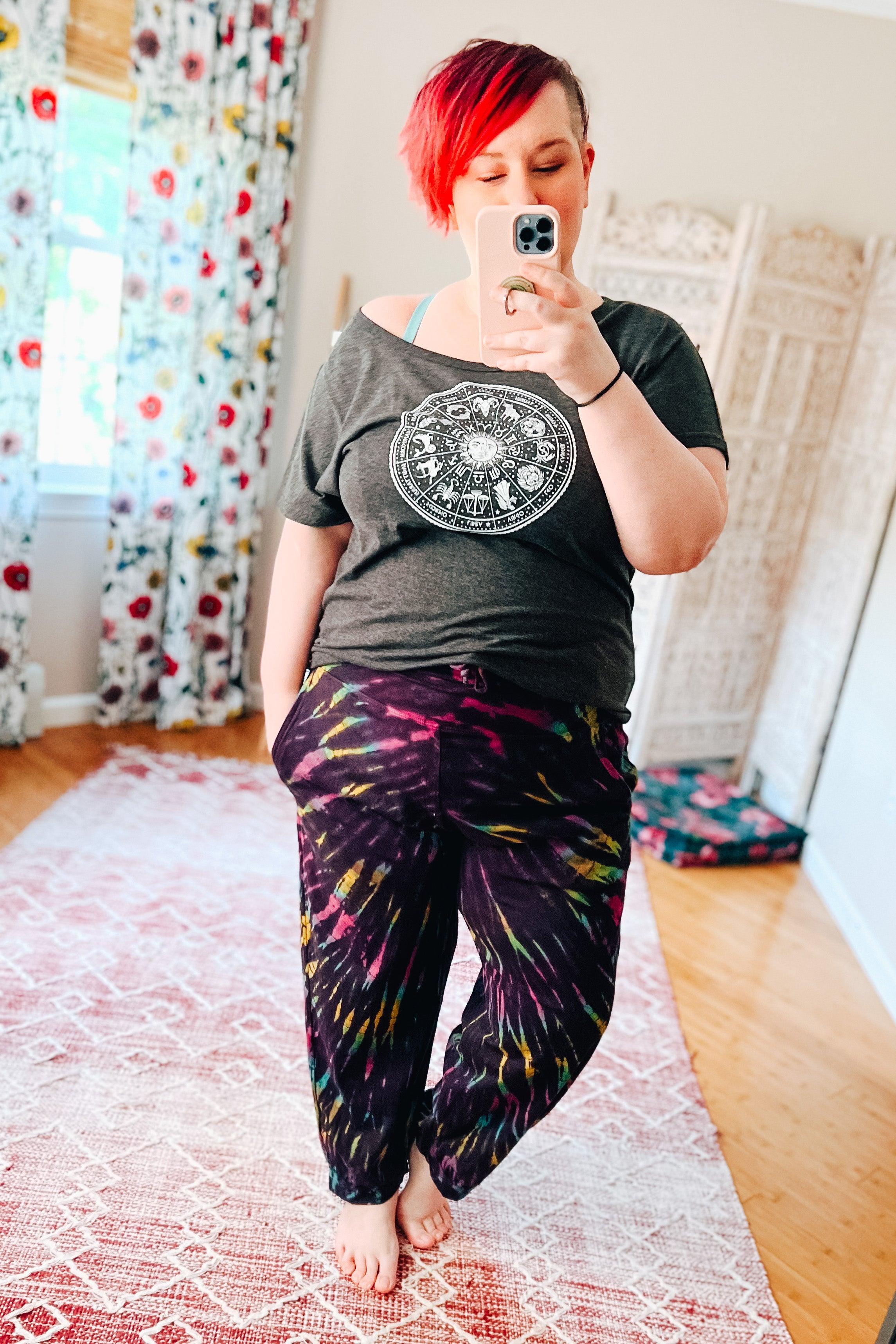Woman wearing purple tie dye joggers paired with a dark graphic tee standing barefoot in a bright bohemian room