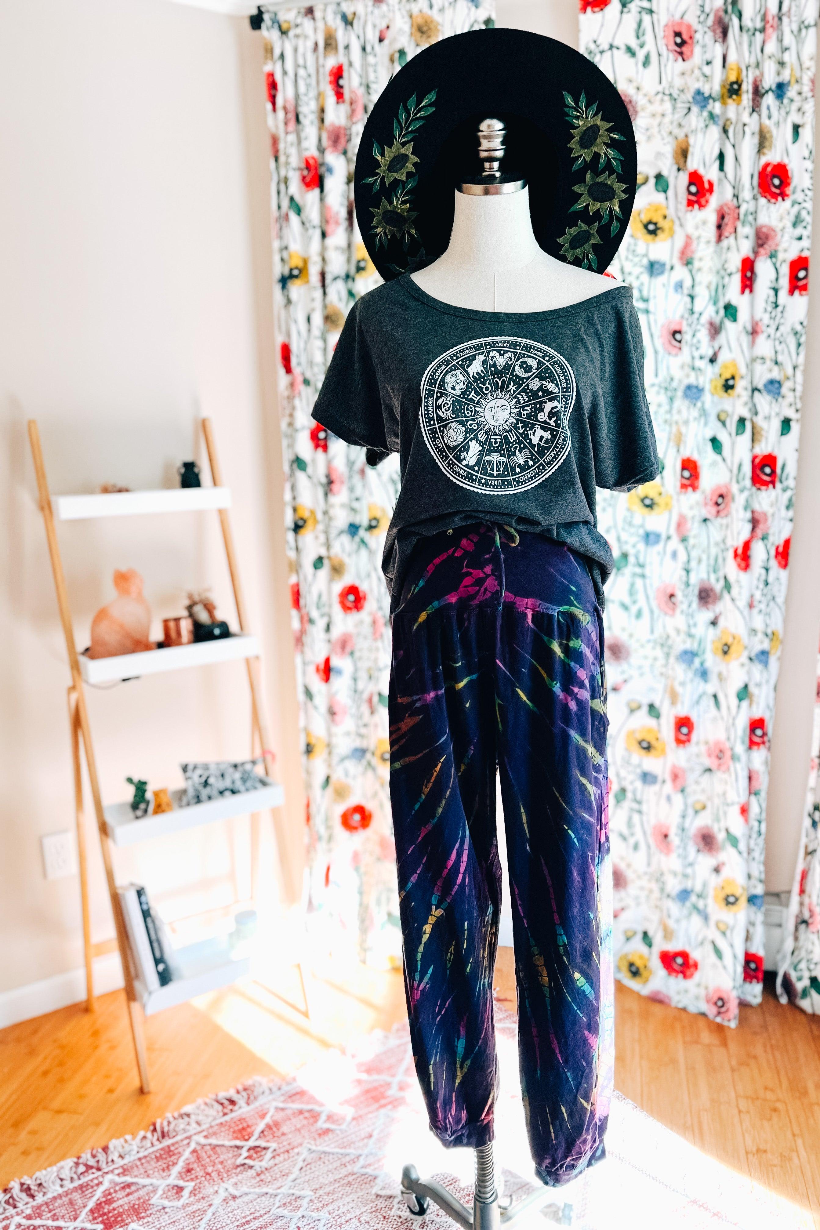 Mannequin wearing black graphic tee with celestial design and colorful tie dye joggers in bright floral room setting