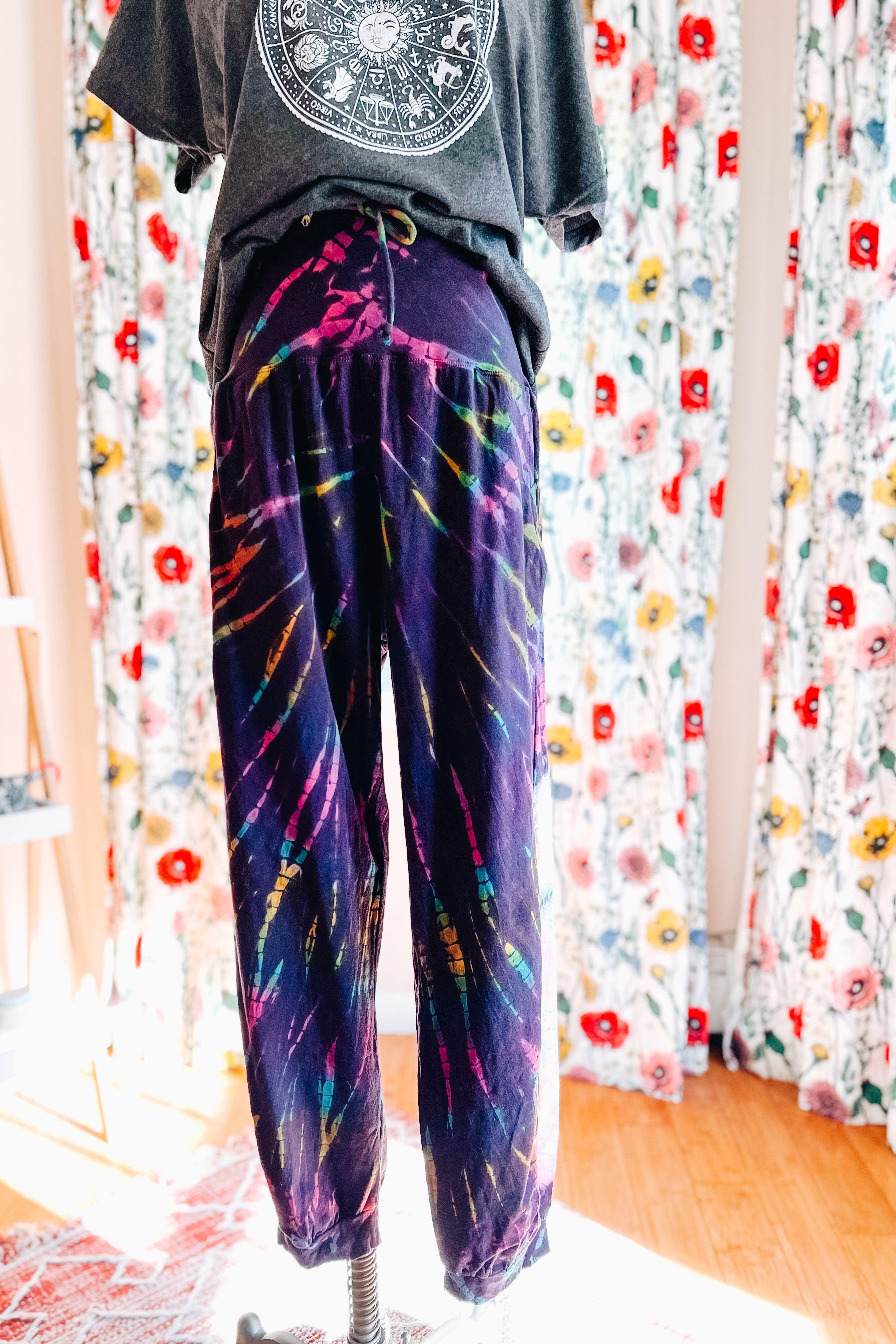 Vibrant purple tie dye joggers with relaxed fit displayed indoors against floral curtains on dress form