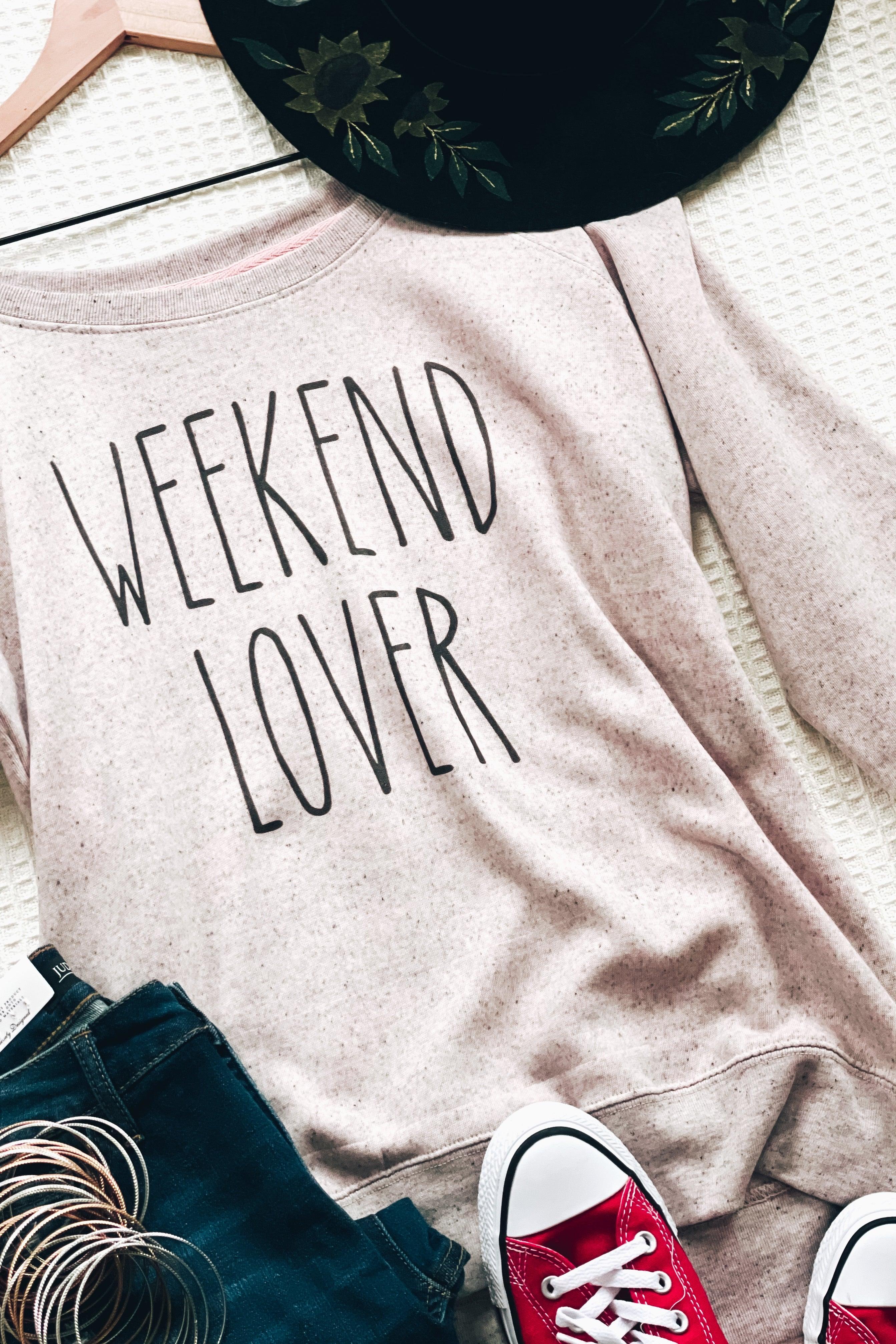 Blush scoop neck pullover with "Weekend Lover" text paired with dark jeans and red sneakers on textured surface