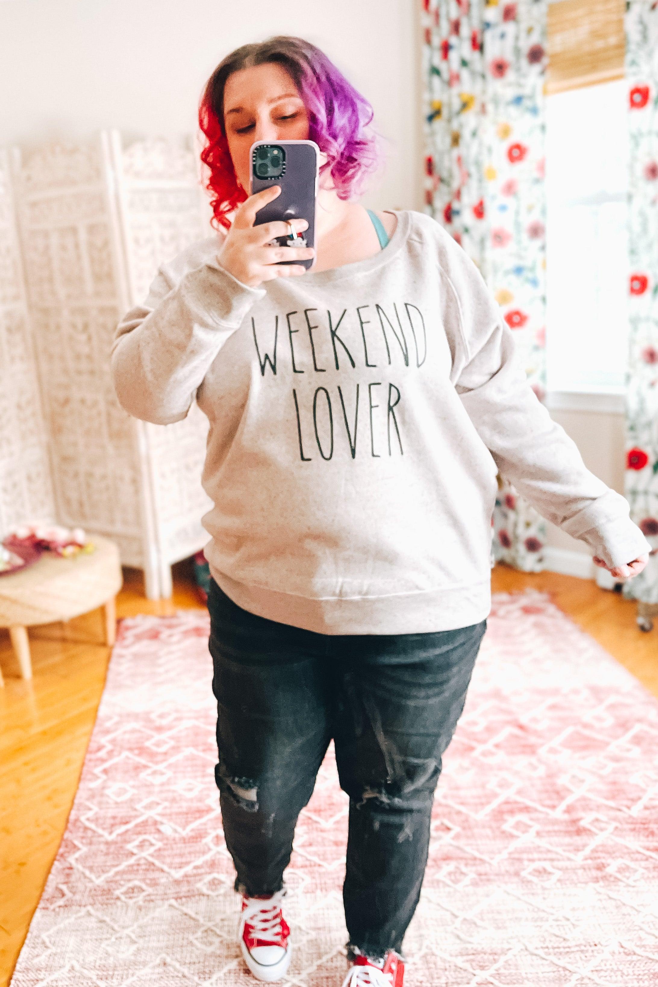 Plus-size woman with vibrant purple and red hair wearing relaxed scoop neck pullover and black distressed jeans indoors