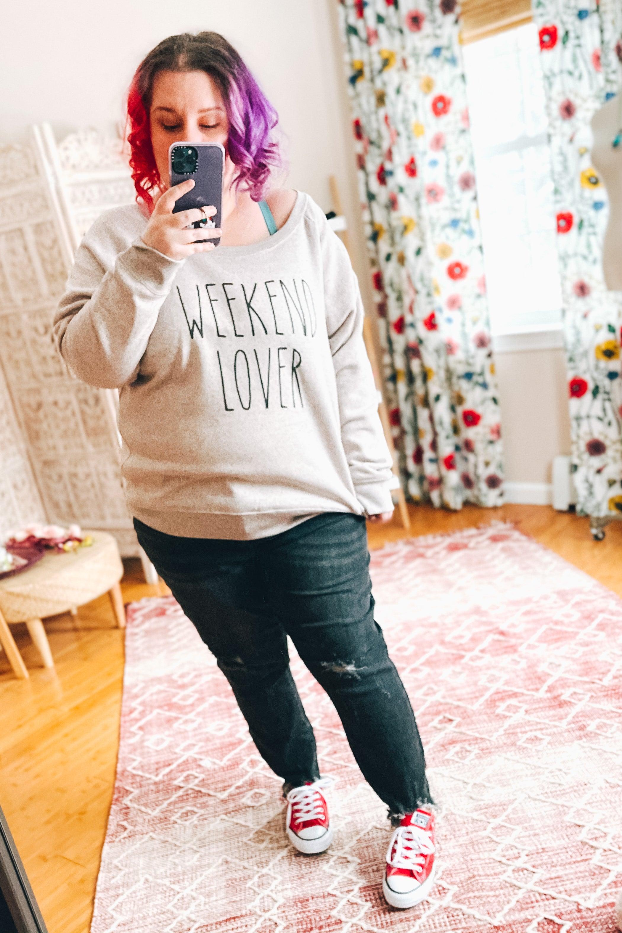 Woman with colorful hair wearing blush relaxed scoop neck pullover and black jeans taking mirror selfie indoors