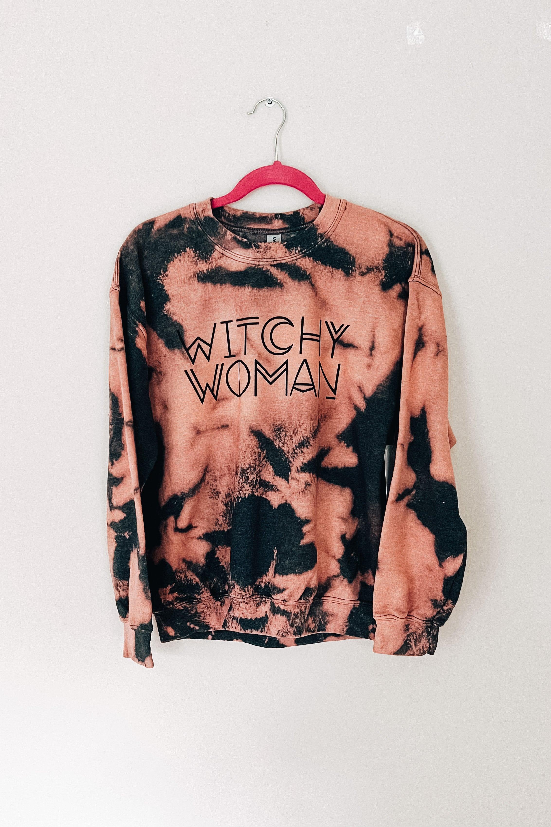 Charcoal and pink bleached sweatshirt with "Witchy Woman" text hanging on pink hanger against white wall