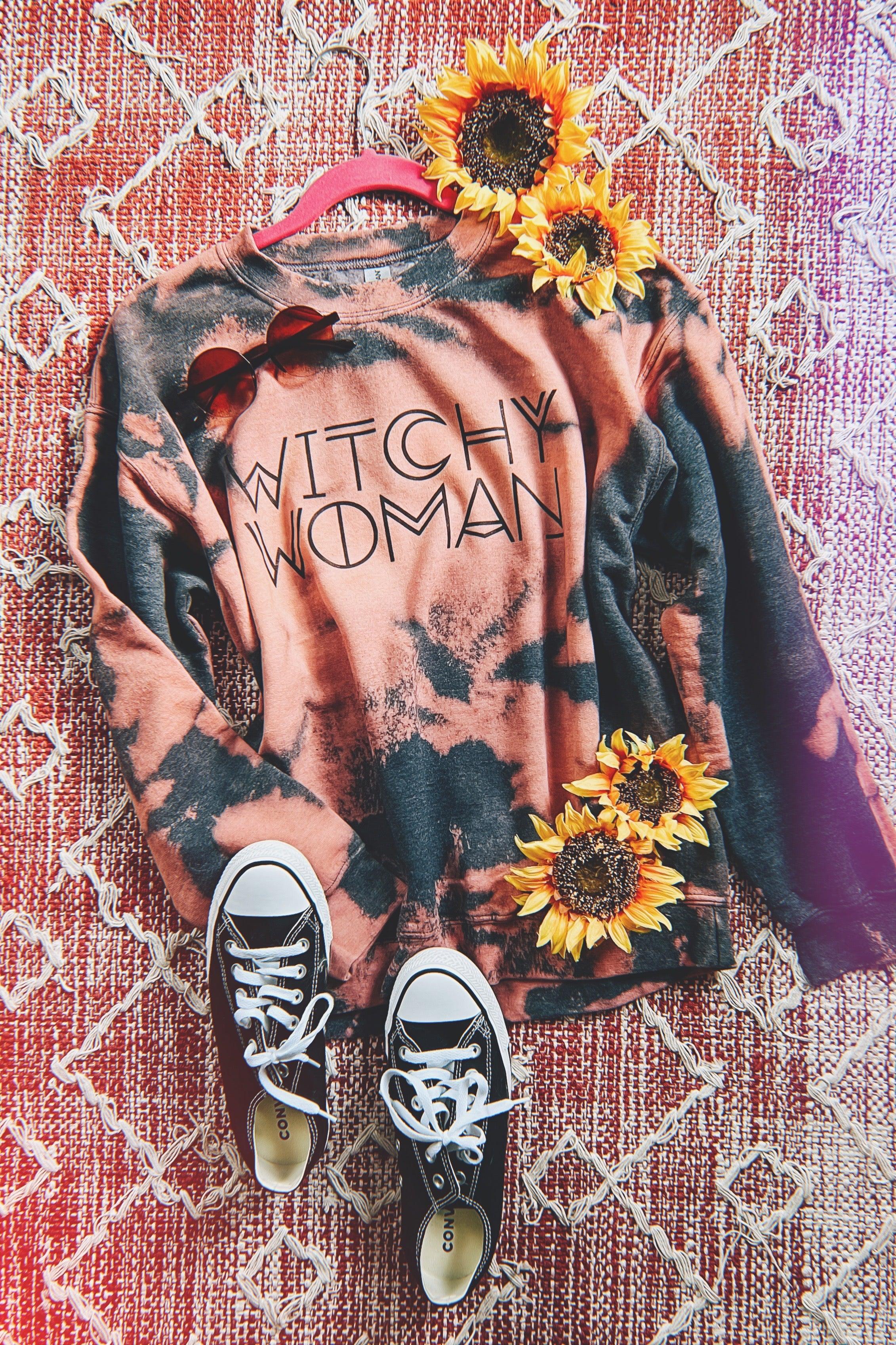Charcoal and pink bleached sweatshirt with "Witchy Woman" text, paired with black sneakers and sunflowers on patterned rug