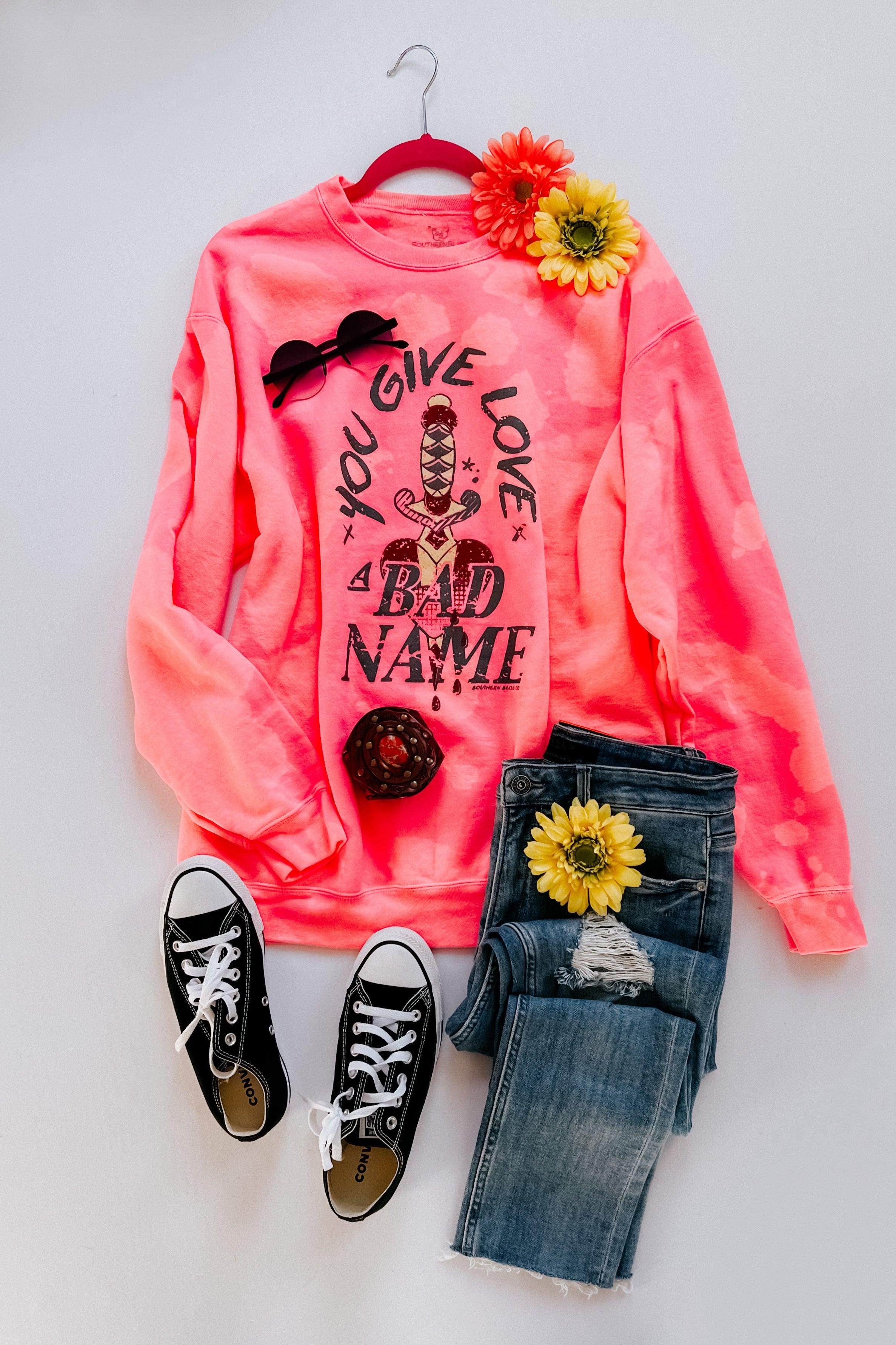 Bright pink bleached pullover with bold graphic text styled with ripped jeans, black sneakers, and floral accents