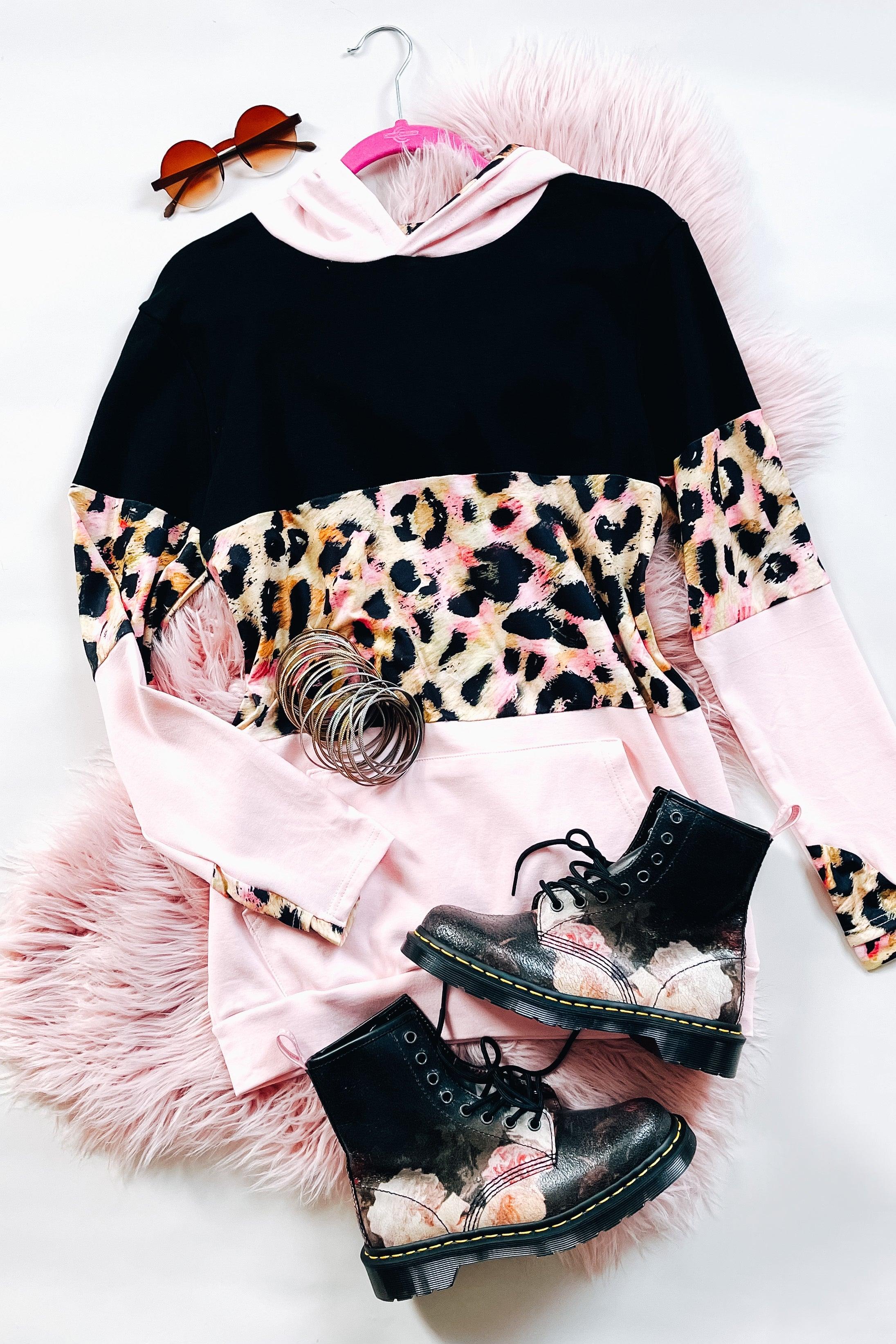 Black and pink hoodie with leopard print detail styled with metallic combat boots and round sunglasses on pink fur rug