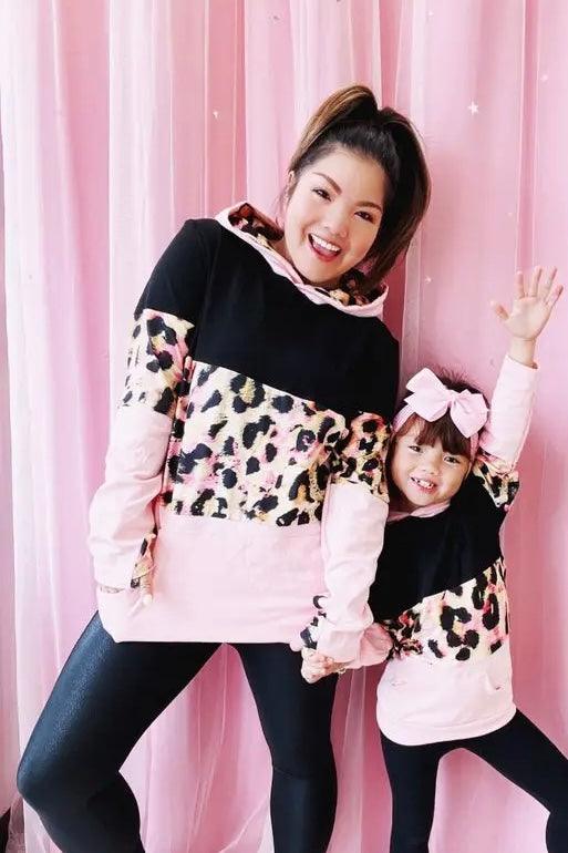 Woman and child wearing matching black, pink, and leopard print hoodies posing happily against pink backdrop