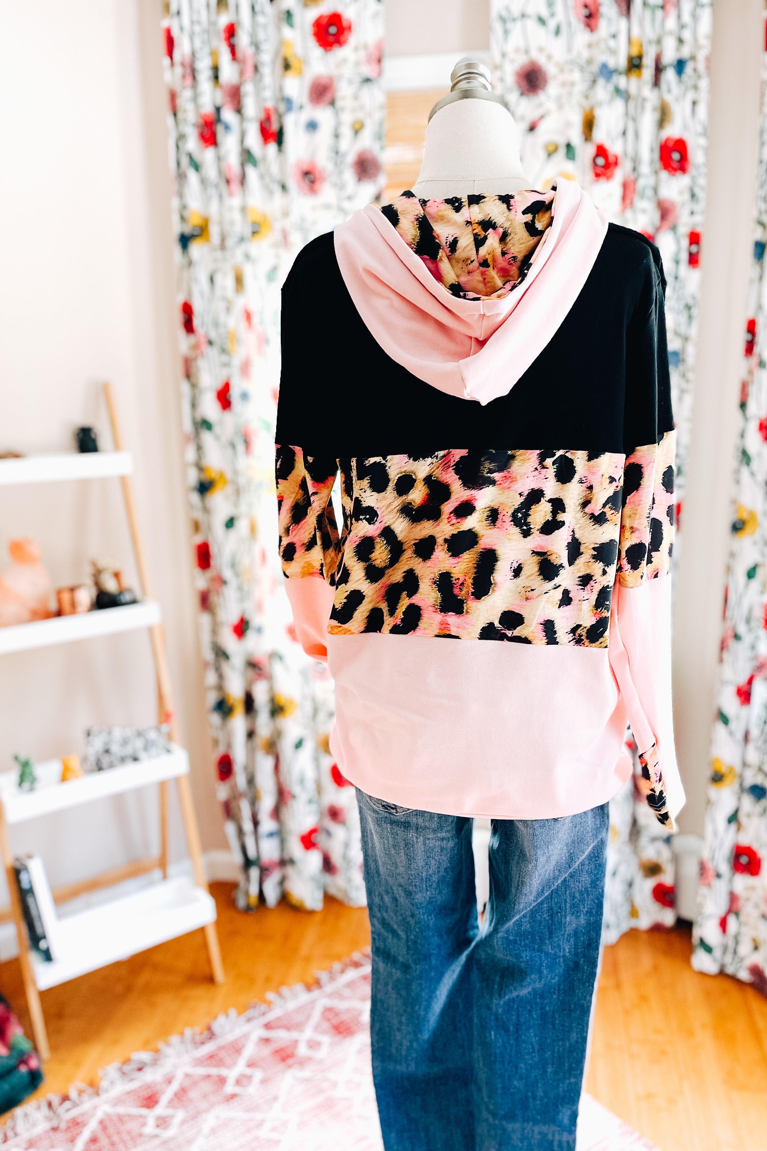Back view of black and pink color block hoodie with leopard print panel styled with blue jeans in cozy indoor setting