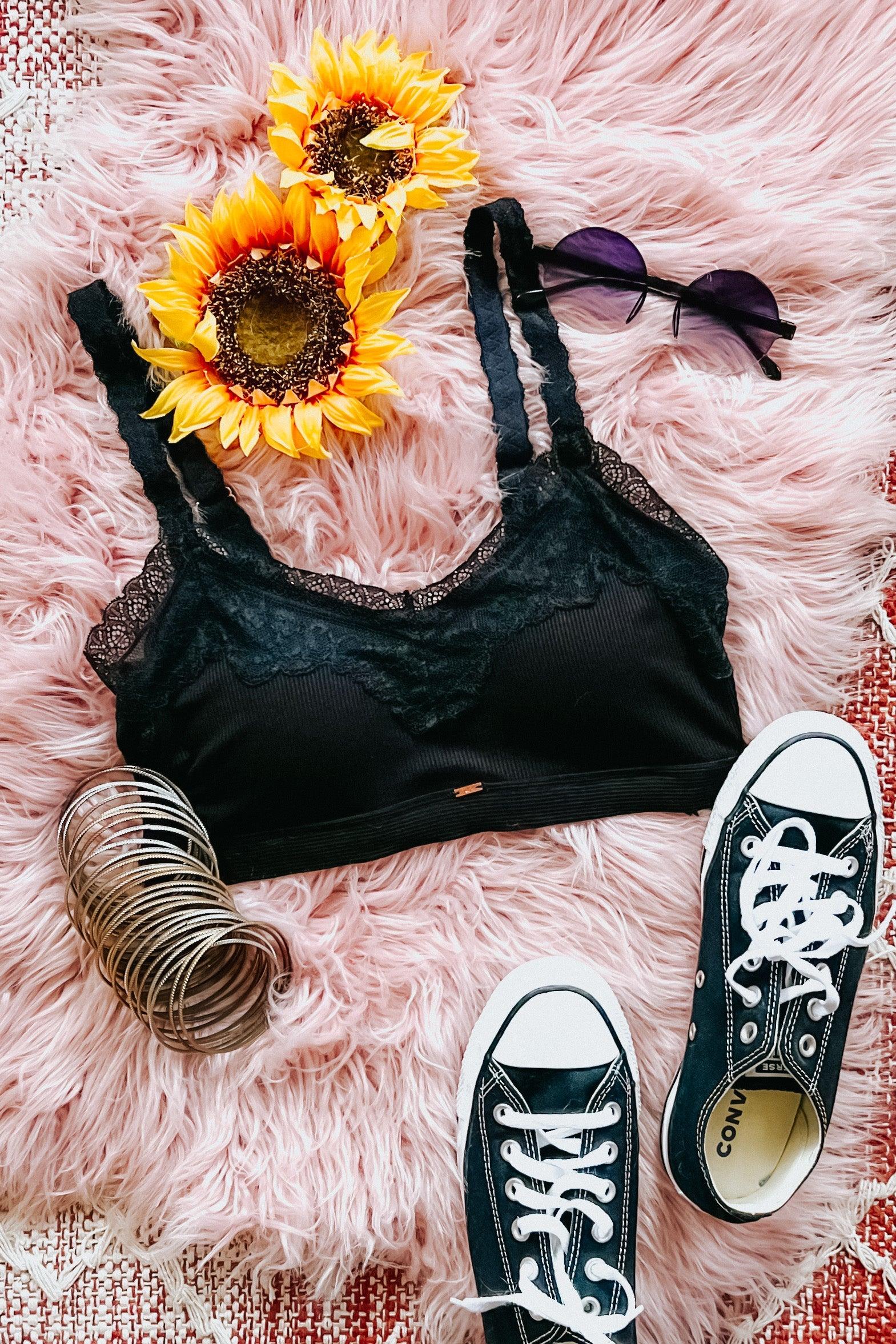 Black lace-trim bralette styled with sunflowers, silver bangles, round sunglasses, and black Converse sneakers on pink fur rug