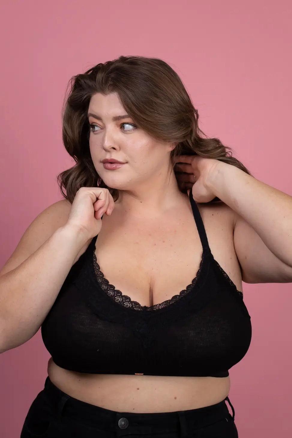 Plus-size woman wearing black lace-trim bralette with adjustable straps posing against pink background