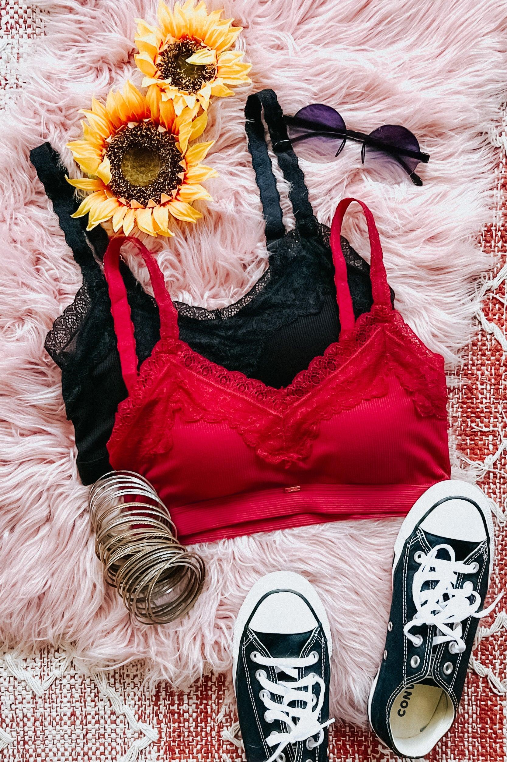 Wine-colored lace trim bralette paired with black lace bralette, black sneakers, bracelets, and sunglasses on pink rug