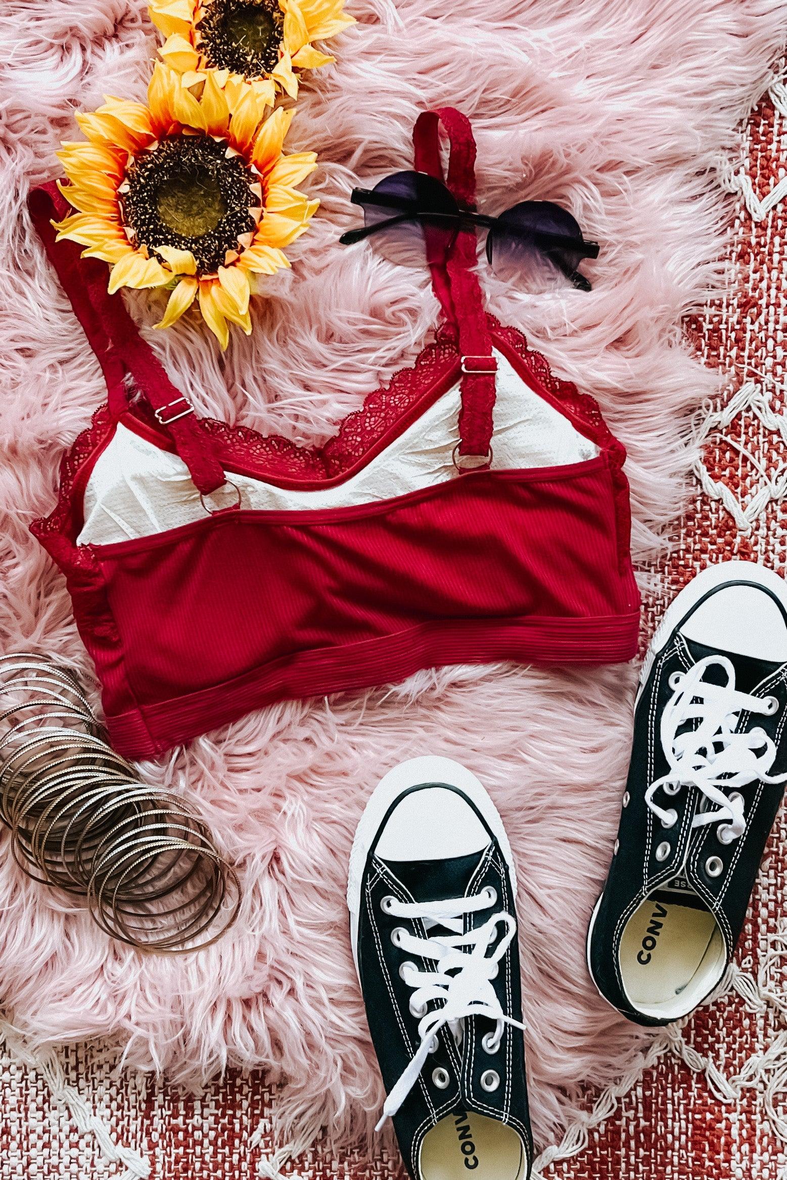 Wine-colored lace trim bralette with adjustable straps styled with sunflowers, black sunglasses, bracelets, and black sneakers on pink fur